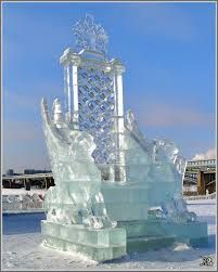 an ice sculpture in front of a building with snow on the ground and blue sky