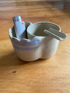 a ceramic cup with a toothbrush holder and lighter in it on a wooden table