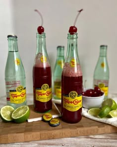 three bottles of soda sit on a cutting board with limes and cherries around them