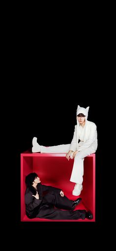 two people dressed in white sitting on a red box with one person laying down and the other standing up