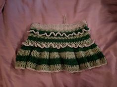 a green and white crocheted skirt laying on top of a pink bed sheet