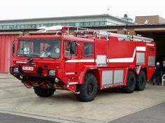 a large red fire truck parked in front of a building with people standing around it