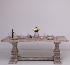 a wooden table topped with pink plates and bowls next to a vase filled with flowers