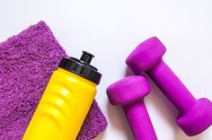 two purple dumbs and a yellow water bottle next to each other on a white surface