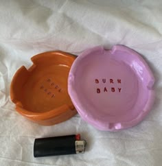 two orange and pink bowls with the words burn baby written on them next to a lipstick bottle