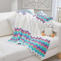 a crocheted blanket is sitting on a couch with an owl stuffed animal next to it