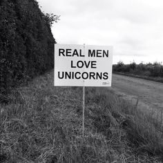 a real men love unicorns sign sitting in the middle of a grass covered field