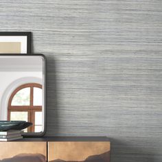 a mirror sitting on top of a wooden dresser next to a wall mounted shelf filled with books