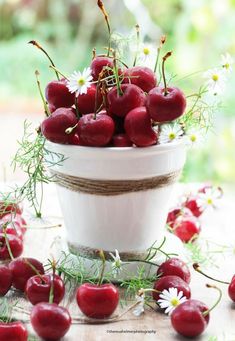 a bowl filled with cherries and daisies on top of a wooden table next to flowers