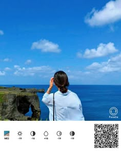 a woman looking out at the ocean while holding her hand up to her face with an island in the background