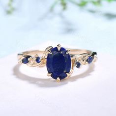 an oval shaped blue sapphire ring set in yellow gold with leaves around the band and side stones