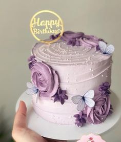 a hand holding a cake with purple frosting and butterflies on it that says happy birthday