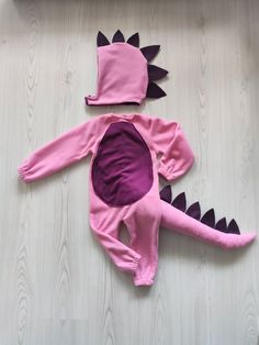 a baby's pink and purple dinosaur costume laying on top of a wooden floor