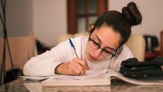 a woman in glasses is writing on paper