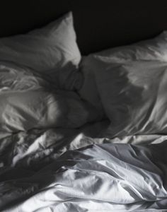 an unmade bed with white sheets and pillows