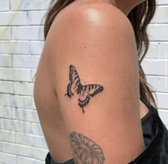 a woman with a butterfly tattoo on her arm and shoulder, standing in front of a brick wall