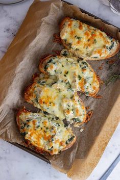 two pieces of bread with cheese and herbs on it sitting on a piece of wax paper