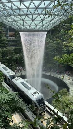 a train is passing by a waterfall in the middle of a tropical area with people walking around