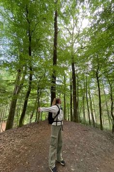 a woman standing in the middle of a forest pointing at something with her hand on her hip