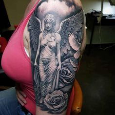 a woman with an angel tattoo on her arm and shoulder is sitting in front of roses