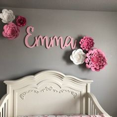 a white crib with pink and white flowers hanging on the wall next to it