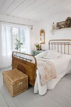 a bedroom with white walls and flooring has a metal bed frame, wicker basket on the footboard