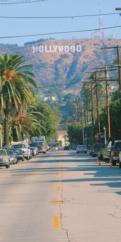 cars parked on the side of a road with hollywood sign in the background and palm trees lining the street