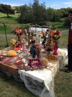 a man standing next to a table filled with food and drinks on top of a lush green field