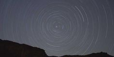 star trails in the night sky with mountains and rocks behind them, as seen from below