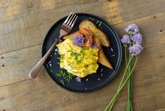 an omelet with toast and flowers on a black plate next to a fork