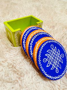 four blue and orange frisbees sitting next to a green box on a white carpet