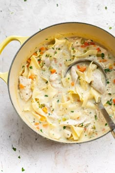 a pot filled with chicken noodle soup on top of a white counter next to a spoon