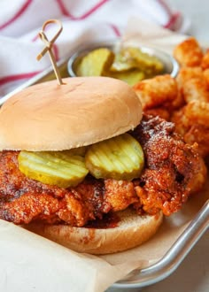 a chicken sandwich with pickles and sauce on a bun next to some fried food