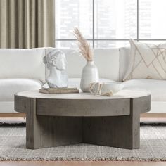 a living room with a couch, coffee table and vase on the floor in front of a window