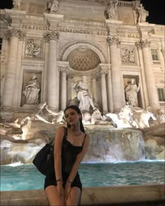 a woman standing in front of a fountain at night with her hand on her hip