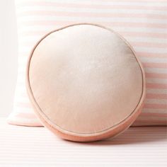 a round pillow sitting on top of a pink and white striped bed sheet next to two pillows