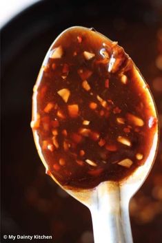 a spoon full of food sitting on top of a pot filled with liquid and sauce