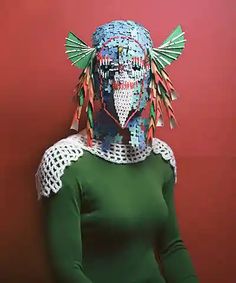 a woman in green shirt standing next to red wall with paper art on her head