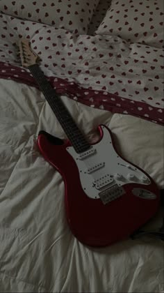 a red electric guitar laying on top of a bed next to a white comforter