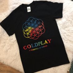 a black t - shirt with the word coldplay on it sitting on a white rug