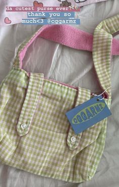 a pink and green bag with a tag on it's side sitting on a bed