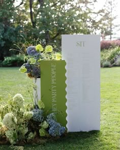 a sign sitting on top of a lush green field next to flowers and plants in vases