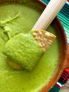 a bowl filled with guacamole and tortilla chips next to a wooden spoon