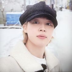 a woman wearing a black hat and white sweater standing in the middle of a snow covered street