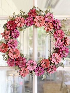 a wreath with pink flowers hanging from the side of a window in front of a door