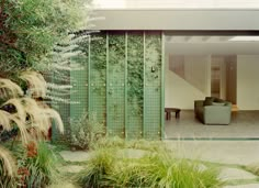 an open living room and dining area with green glass panels on the wall, grass in the foreground