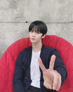 a young man sitting in a red chair making the peace sign with his hand while wearing a white t - shirt and black pants