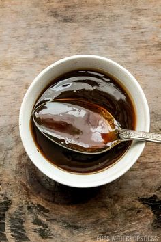 a spoon full of brown liquid sitting in a white bowl on top of a wooden table