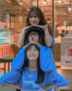 three young women sitting on top of each other in front of a storefront window