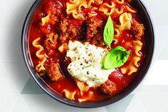 a bowl filled with pasta and meat on top of a white tiled countertop next to a spoon